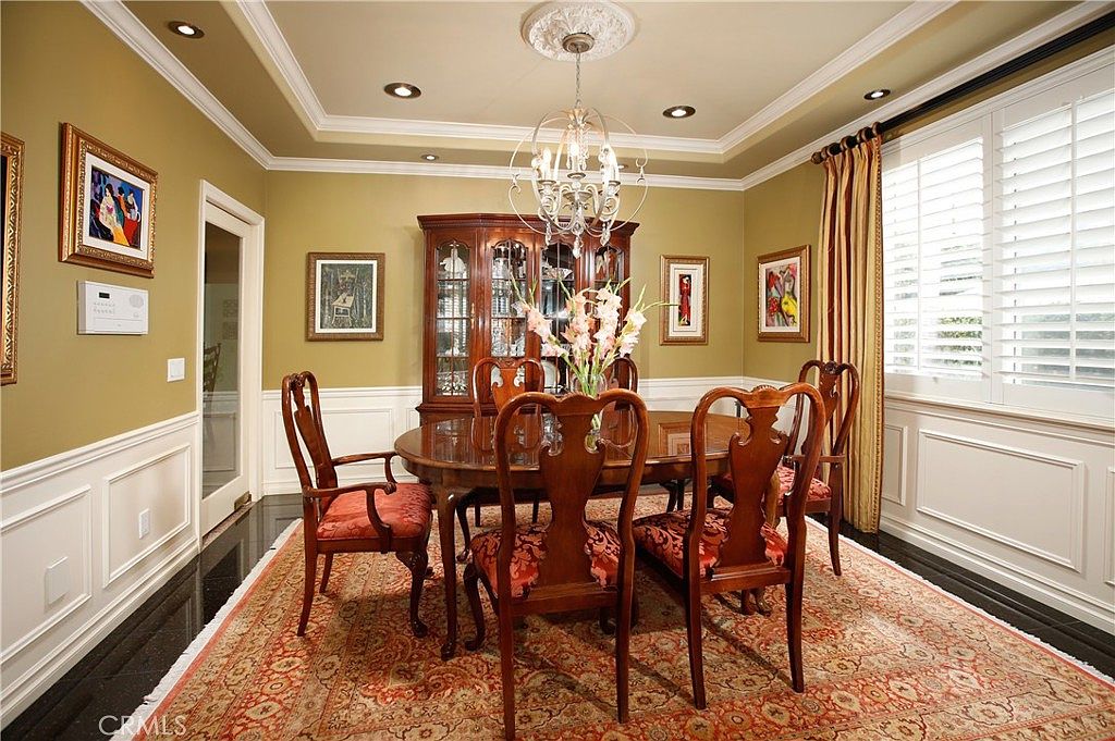 The formal dining room with coffered ceiling, wainscoting, and a chandelier above a cherry table