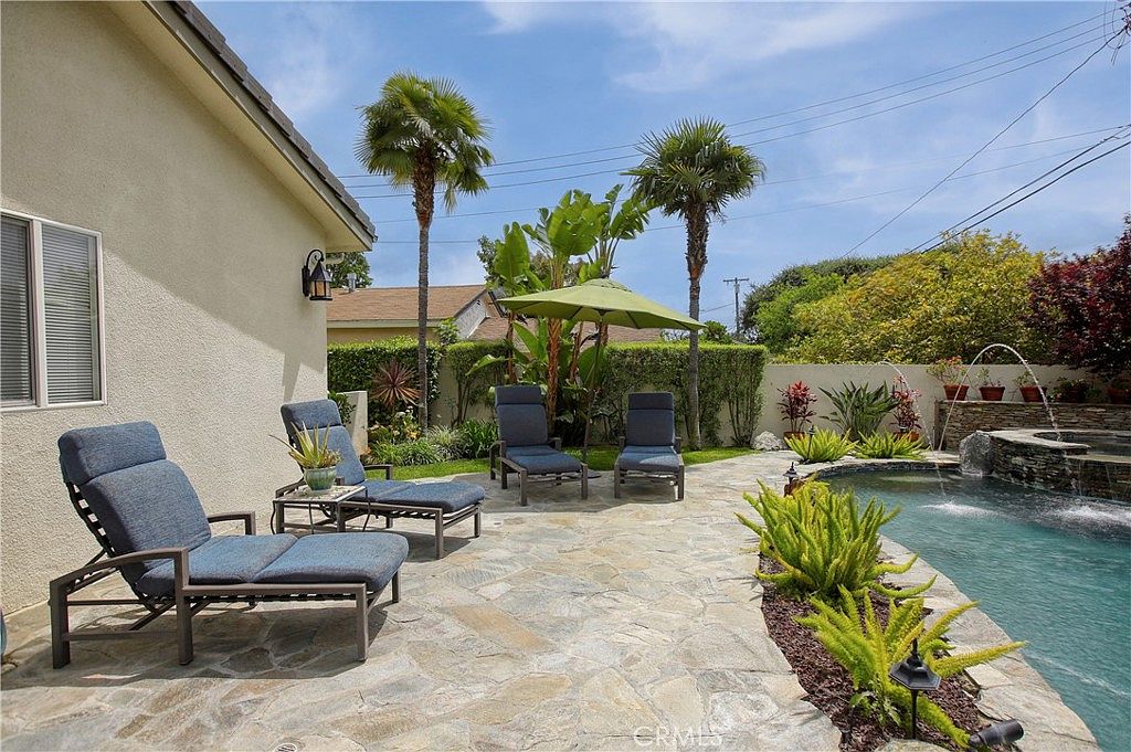 Pool deck with chaise lounges, palm-shaded loungers, and a water-feature wall